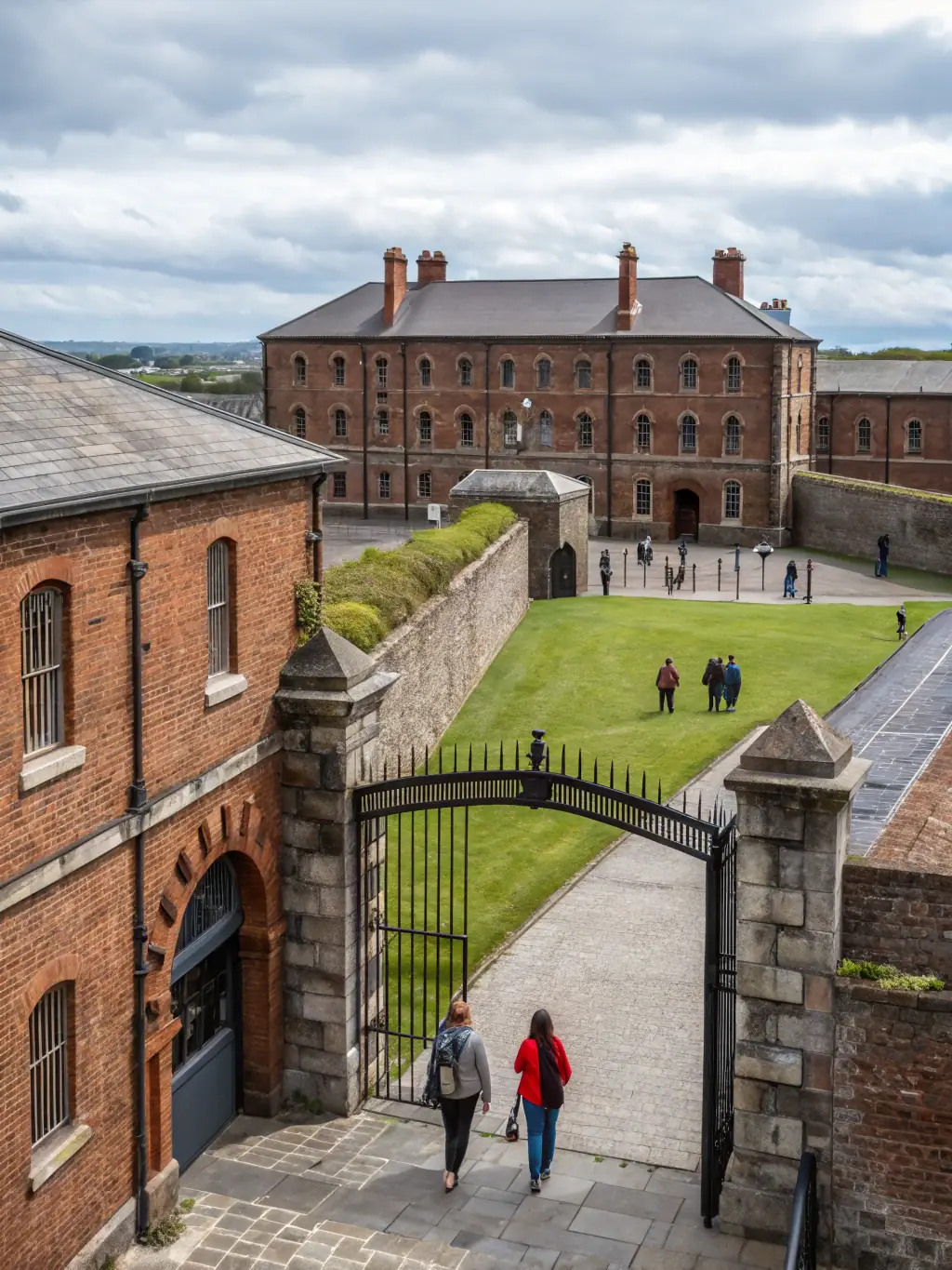 A panoramic view of the Kilmainham Gaol museum, showcasing the architecture and the surrounding landscape, with visitors entering the main gate.